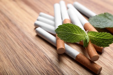 Photo of Menthol cigarettes and mint leaves on wooden table, closeup. Space for text