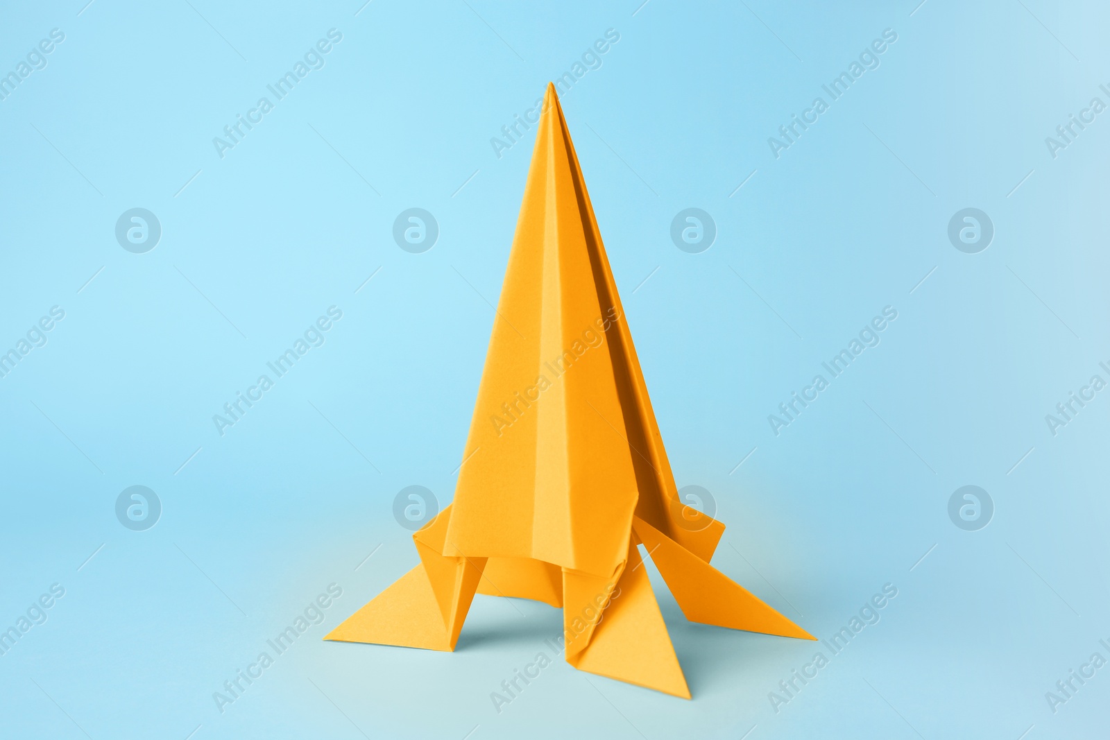 Photo of Origami art. Handmade yellow paper rocket on light blue background