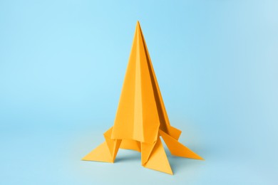 Photo of Origami art. Handmade yellow paper rocket on light blue background