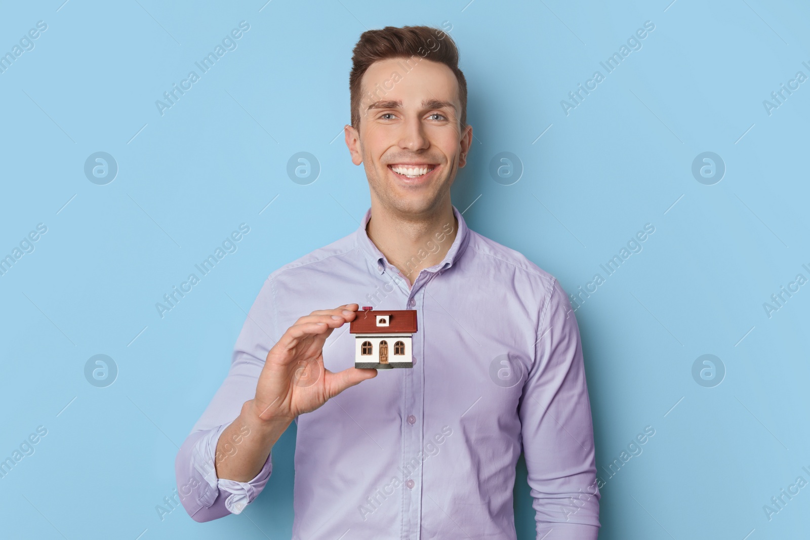 Photo of Male real estate agent with house model on light background