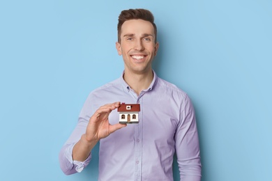 Male real estate agent with house model on light background