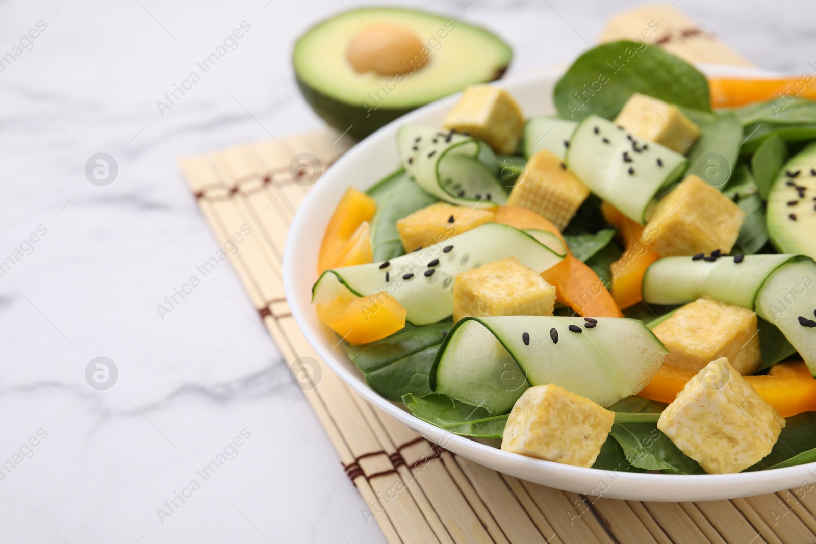 Photo of Bowl of tasty salad with tofu and vegetables on white marble table, closeup. Space for text