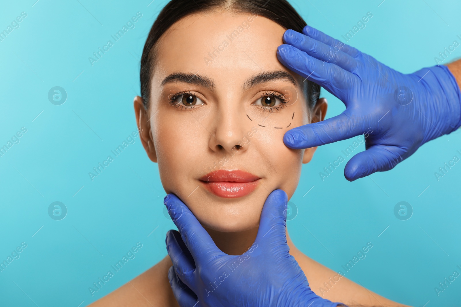 Photo of Doctor checking patient's face before cosmetic surgery operation on light blue background, closeup