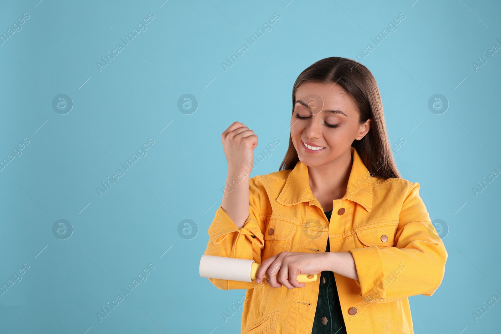 Photo of Young woman cleaning clothes with lint roller on light blue background. Space for text