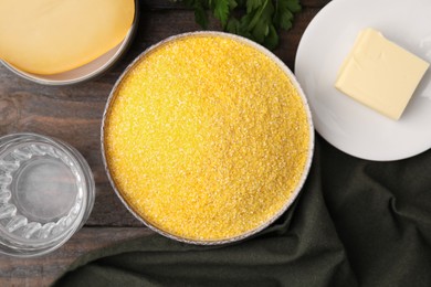 Photo of Raw cornmeal in bowl, water, cheese and butter on wooden table, flat lay