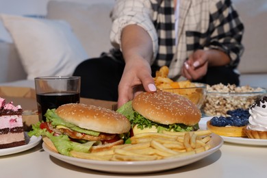 Photo of Overweight woman taking burger at home, closeup