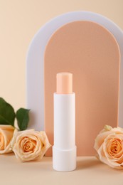 Photo of Stylish presentation of lip balm with rose flowers on beige background