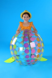 Cute little child in beachwear with inflatable ball on light blue background