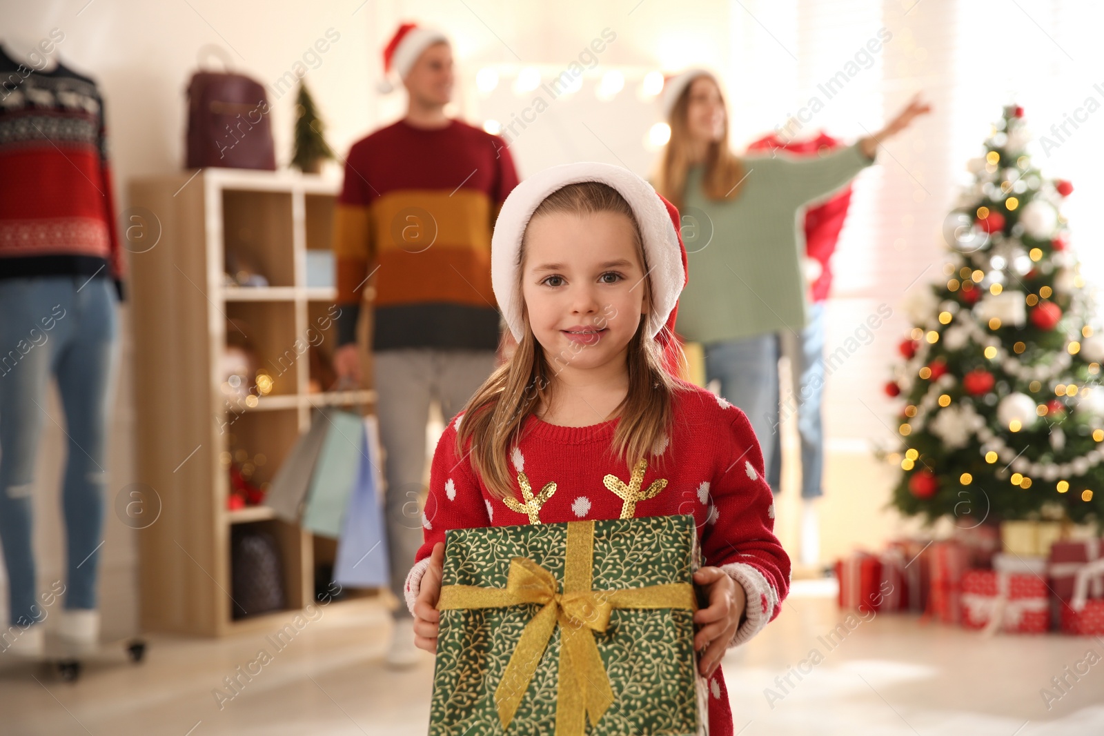 Photo of Little girl with gift box near her parents in store. Family Christmas shopping