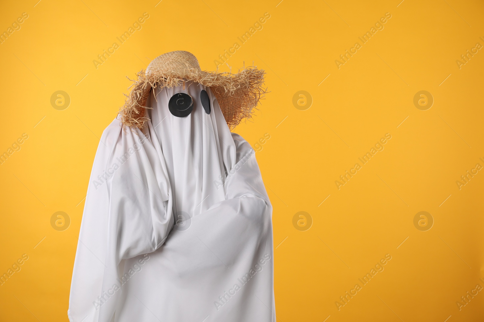 Photo of Person in ghost costume and straw hat on yellow background, space for text