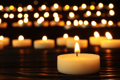 Burning candle on black table against blurred background, space for text
