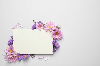 Beautiful chamomile flowers and paper card on white background, flat lay with space for text