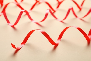 Shiny red serpentine streamers on beige background, closeup