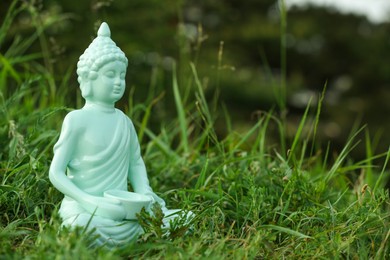 Decorative Buddha statue in green grass outdoors, space for text