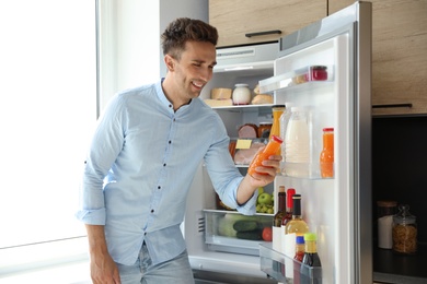 Man with bottle of juice near open refrigerator in kitchen