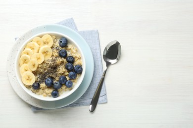 Photo of Tasty oatmeal with banana, blueberries and chia seeds served in bowl on white wooden table, flat lay. Space for text