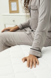 Photo of African American woman sitting on soft mattress in bedroom, closeup