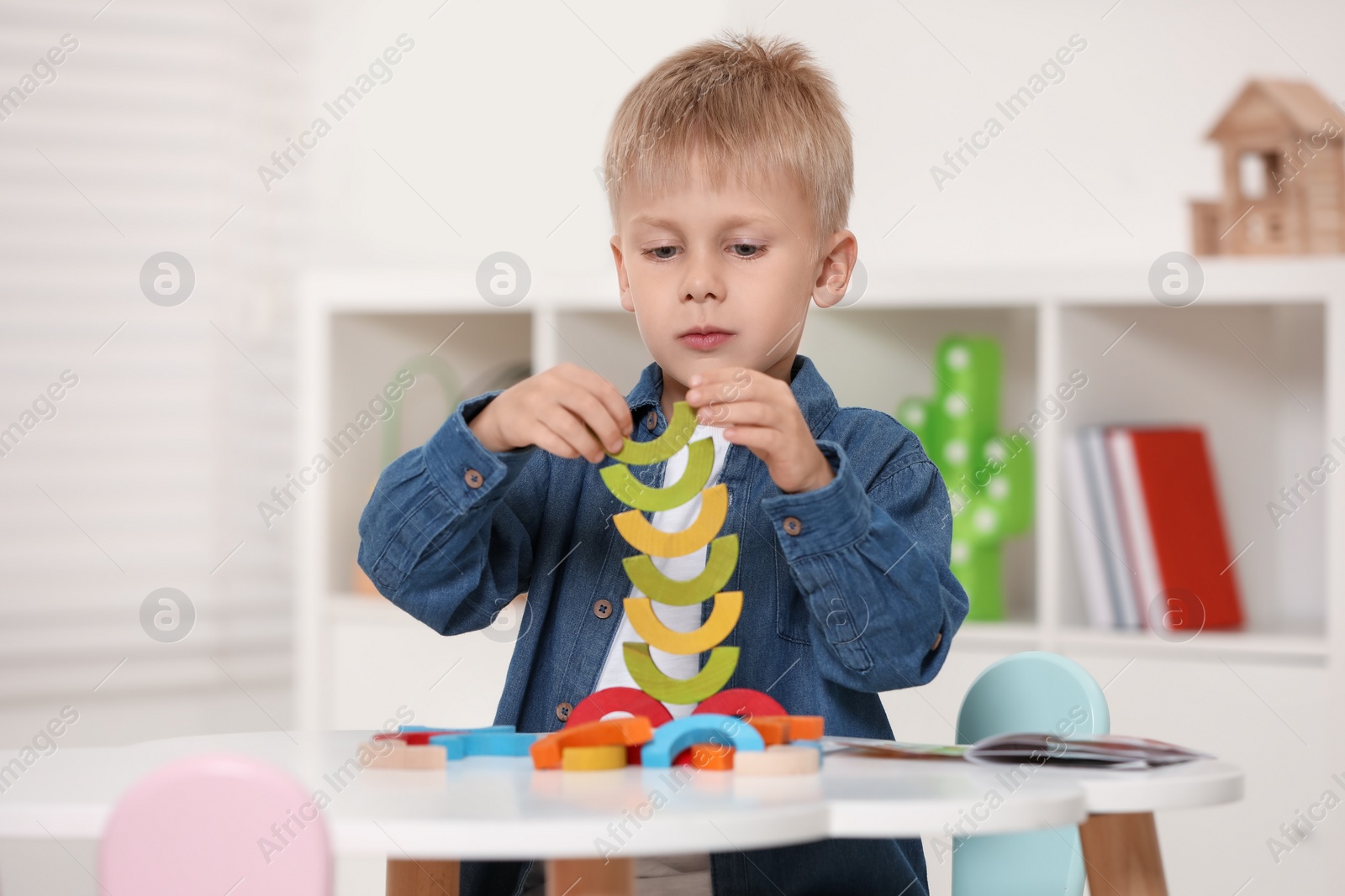 Photo of Cute little boy playing with colorful wooden pieces at white table indoors. Child's toy