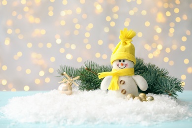 Photo of Snowman toy and Christmas balls on snow against blurred festive lights. Space for text