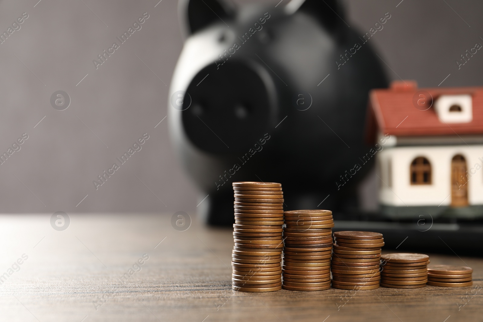 Photo of House model, piggy bank and stacked coins on wooden table, selective focus. Space for text