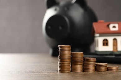 Photo of House model, piggy bank and stacked coins on wooden table, selective focus. Space for text