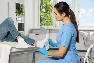 Beautiful female orthopedist examining patient's foot in hospital