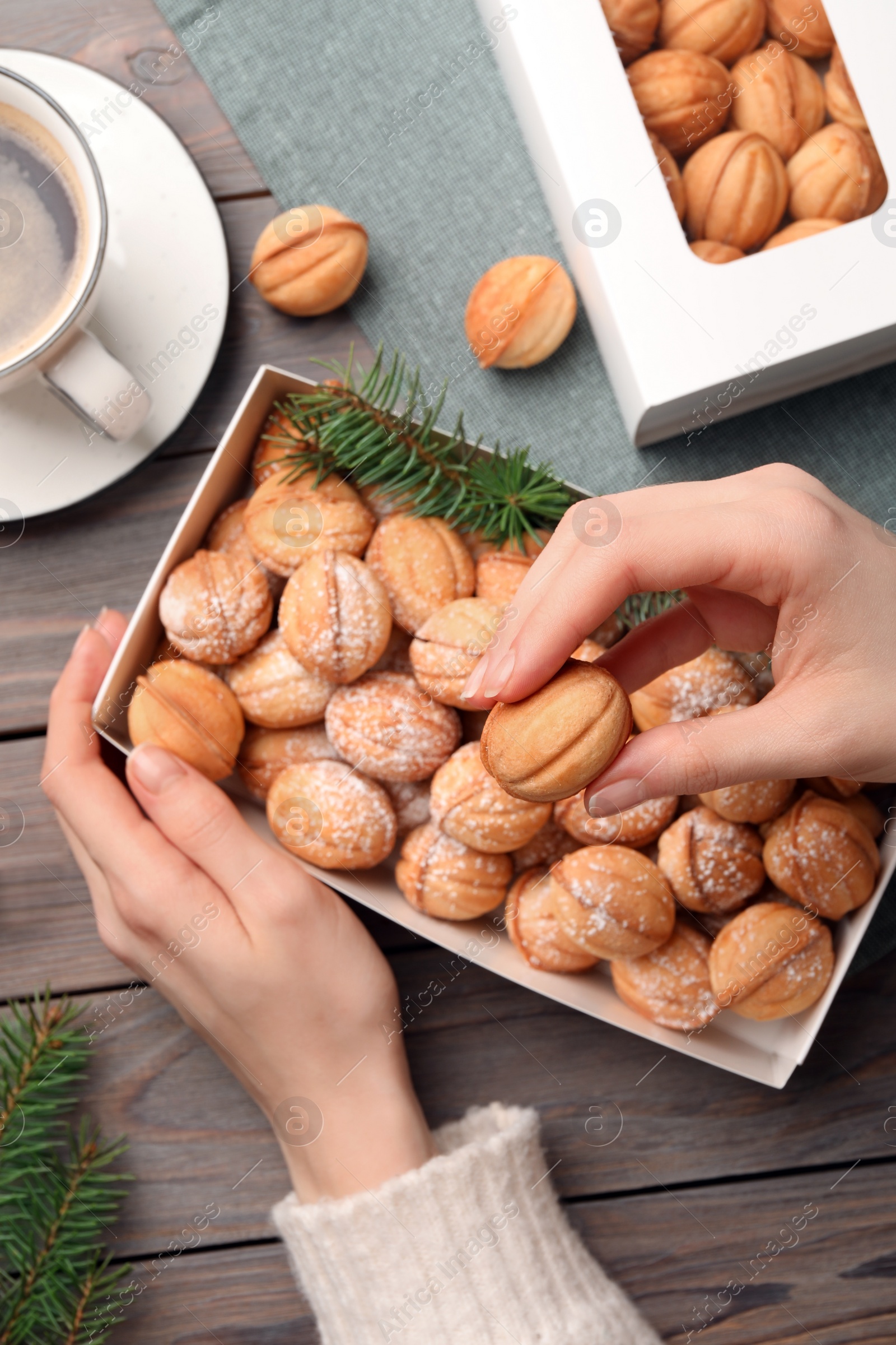 Photo of Woman taking delicious nut shaped cookies from box at wooden table, top view