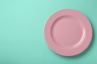 Photo of Clean pink plate on turquoise background, top view. Space for text