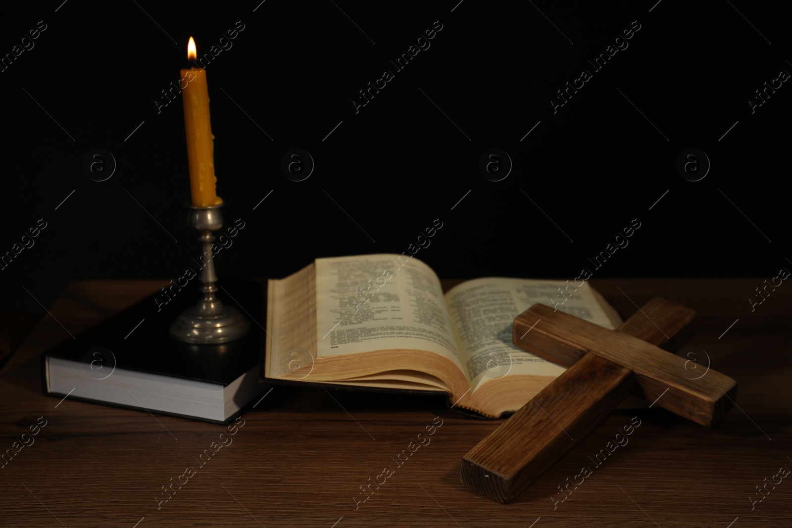 Photo of Church candle, Bible and cross on wooden table against black background