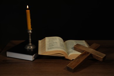 Photo of Church candle, Bible and cross on wooden table against black background