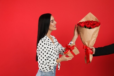 Happy woman receiving tulip bouquet from man on red background. 8th of March celebration