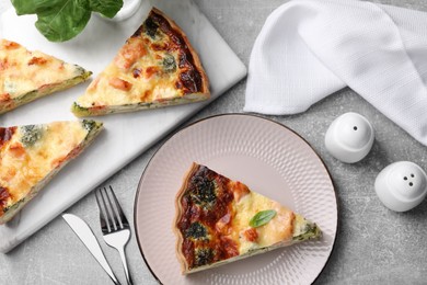 Photo of Pieces of delicious homemade salmon quiche with broccoli, cutlery and shakers on light gray table, flat lay