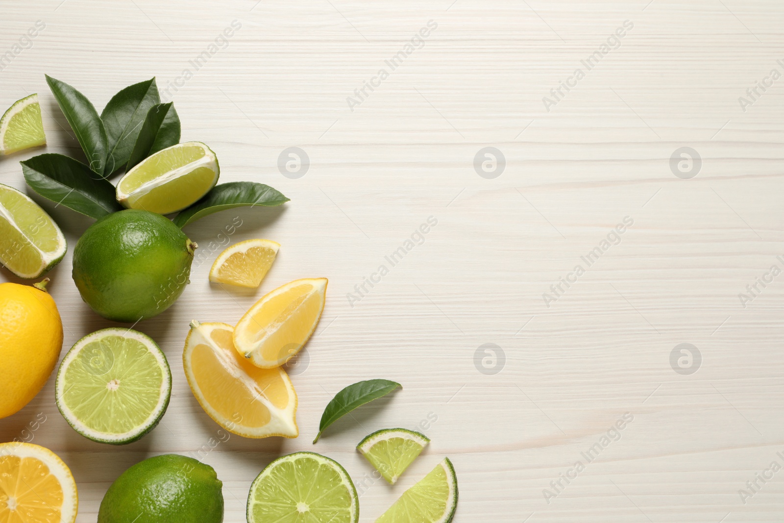 Photo of Fresh ripe lemons, limes and green leaves on white wooden background, flat lay. Space for text