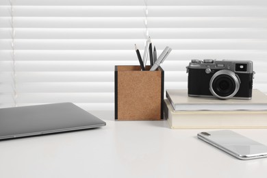Photo of Home office. Laptop, smartphone, vintage camera and stationery on white desk indoors