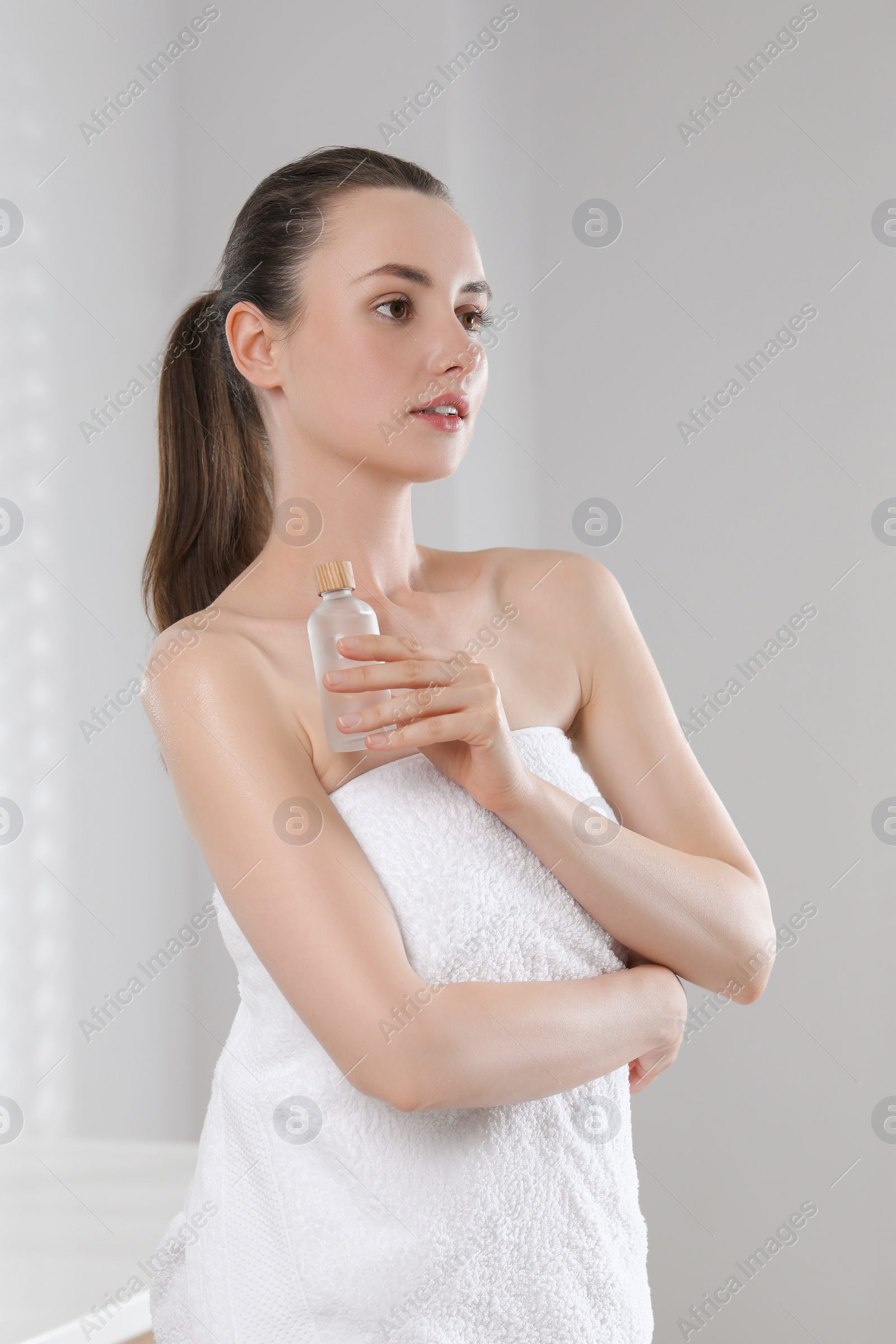 Photo of Beautiful woman with bottle of body oil indoors