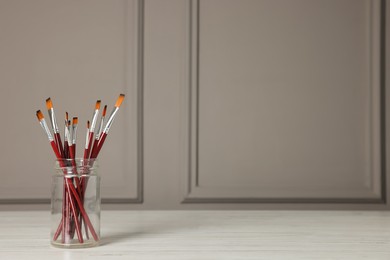 Photo of Set of different paintbrushes in glass jar on white wooden table. Space for text