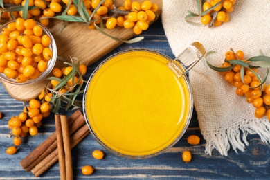 Sea buckthorn tea and fresh berries on blue wooden table, flat lay