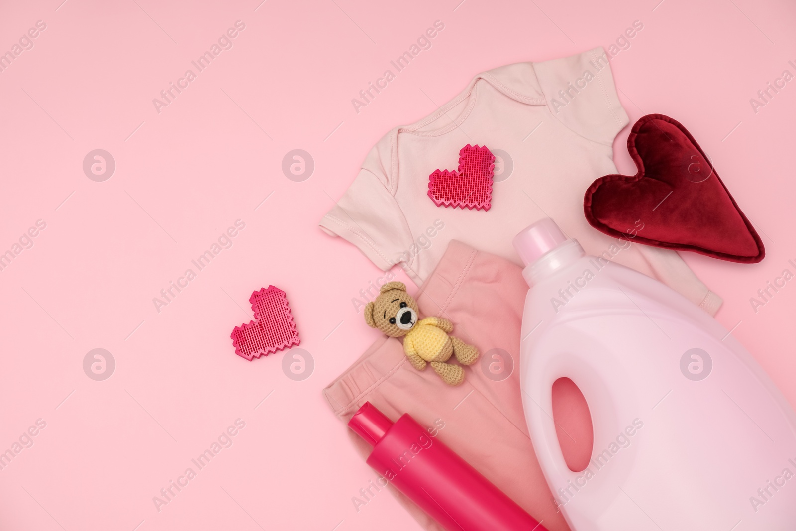 Photo of Bottles of laundry detergents, baby clothes, toy bear and decorative hearts on pink background, flat lay. Space for text