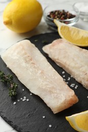 Photo of Fresh raw cod fillets, spices and lemon on white table, closeup