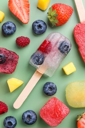 Photo of Different tasty ice pops on pale green background, flat lay. Fruit popsicle