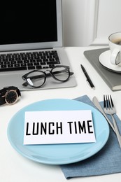 Image of Business lunch. Office desk with plate, cutlery and laptop. Card with phrase Lunch Time on dish