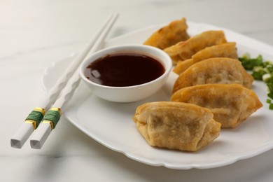 Delicious gyoza (asian dumplings) with soy sauce and chopsticks on white table, closeup