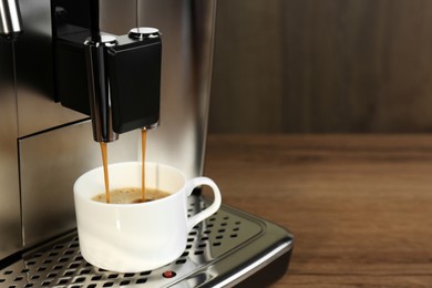 Photo of Modern espresso machine pouring coffee into cup on wooden table, closeup. Space for text