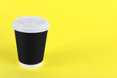 Photo of Black paper cup with plastic lid on yellow background, space for text. Coffee to go