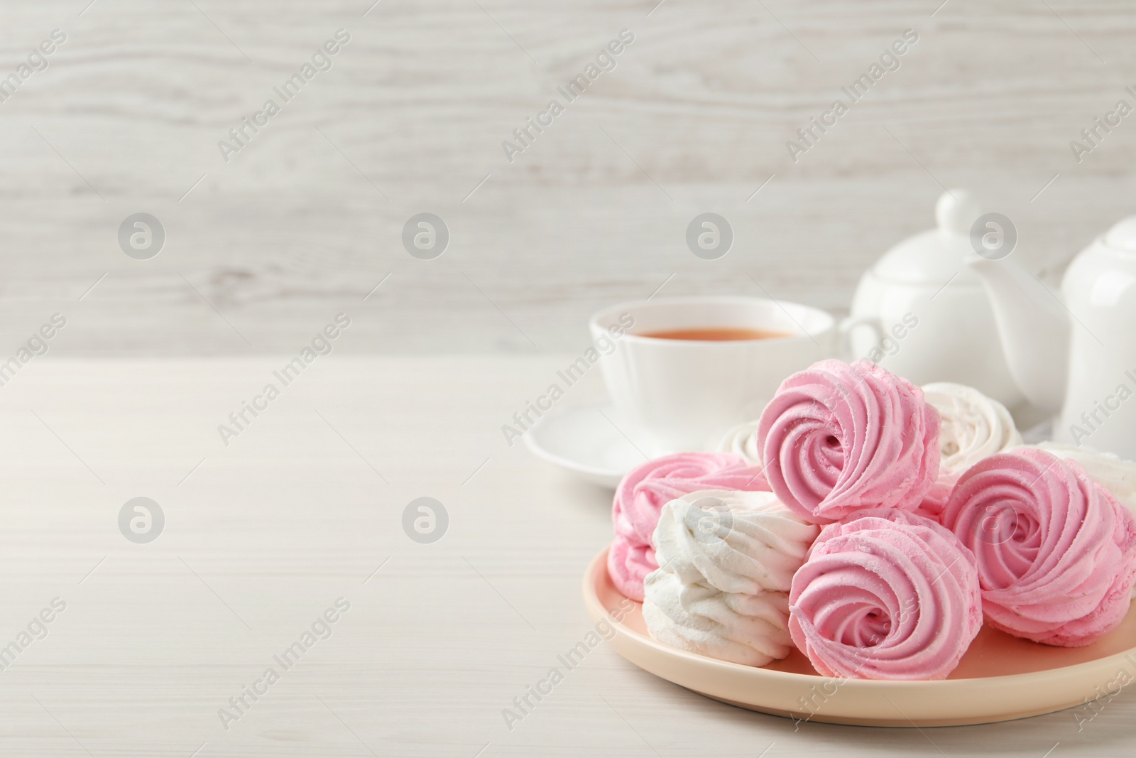 Photo of Delicious zephyrs served with tea on white wooden table, space for text