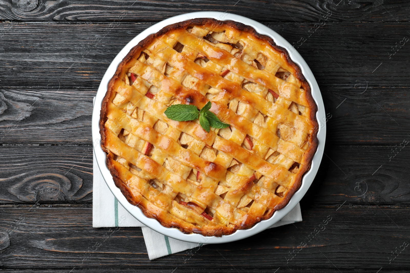 Photo of Traditional apple pie with mint on black wooden table, top view