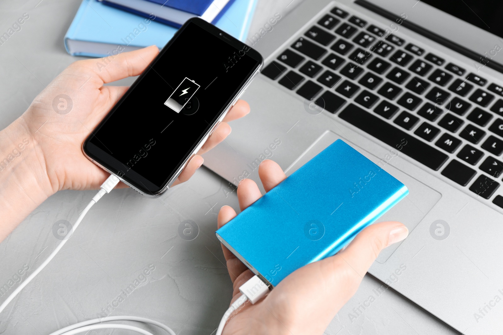 Photo of Woman charging mobile phone with power bank at light grey stone table, closeup