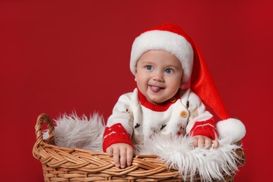 Photo of Cute baby in wicker basket on red background. Christmas celebration