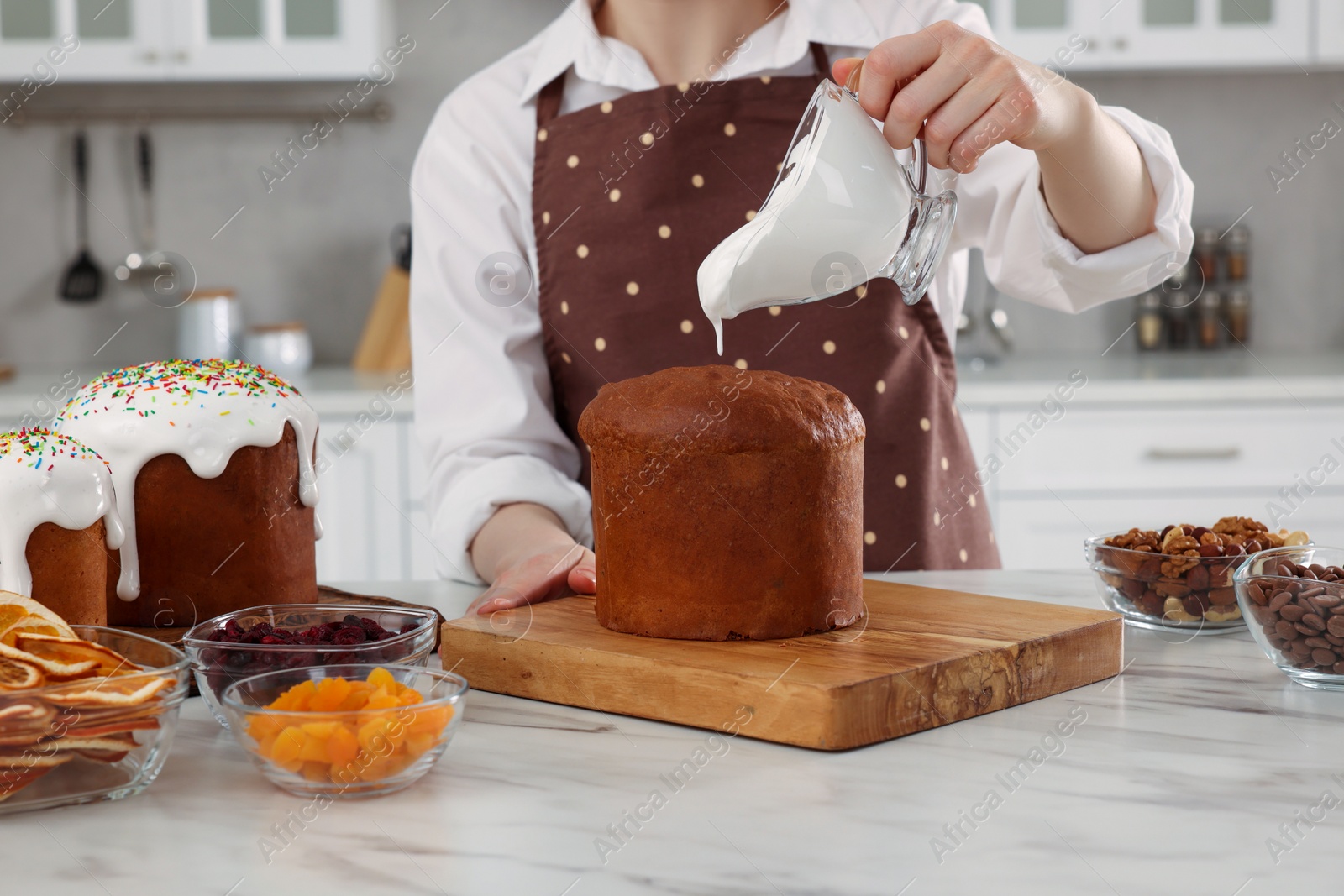 Photo of Woman decorating traditional Easter cake with glaze at white marble table in kitchen, closeup