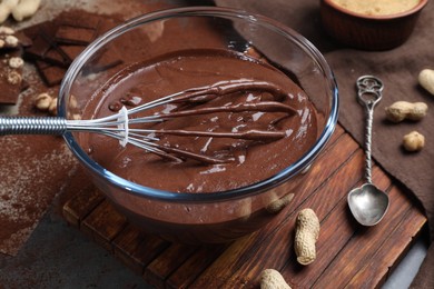 Photo of Bowl of chocolate cream, whisk and spoon on table, closeup